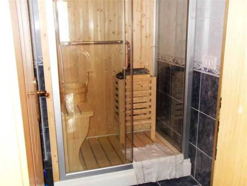 Eine kompakte Heimsauna mit Holzbänken, Ofen und Glastür in einem Badezimmer.