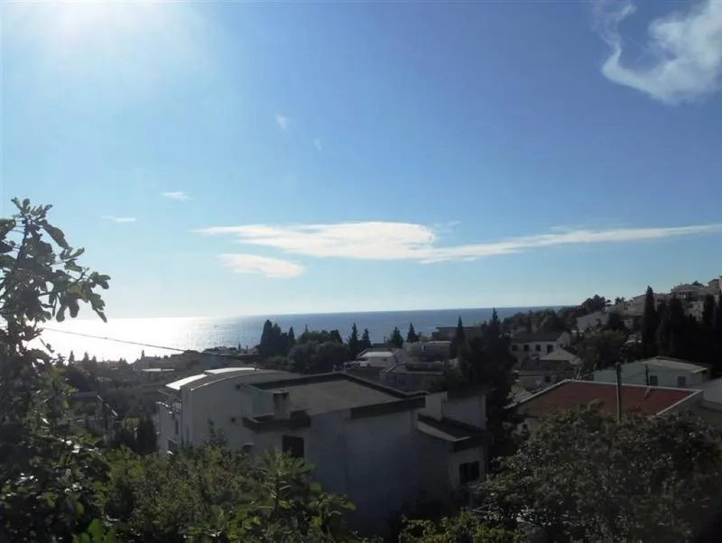 Scenic view of the sea and town with white houses and trees under a clear blue sky.
