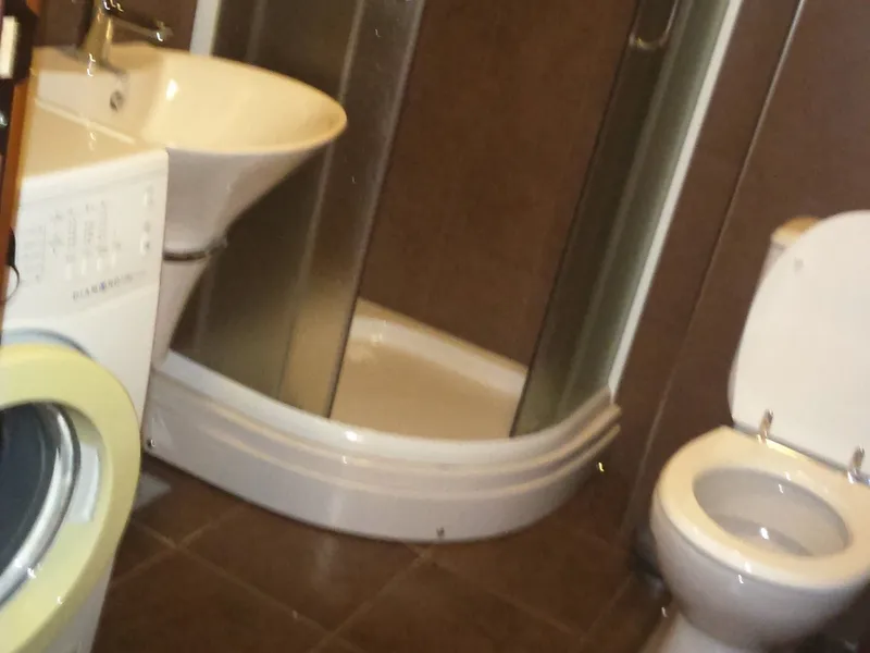 Ein kompaktes modernes Badezimmer mit Duschkabine, Waschbecken, Toilette und Waschmaschine.