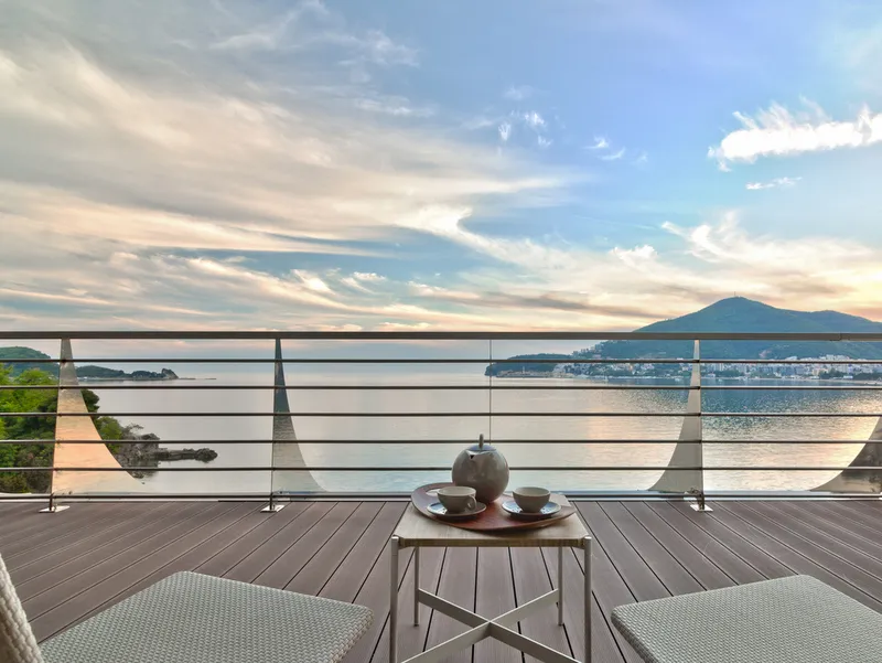 Balkon mit Holzfußboden, Metallgeländer, Beistelltisch mit Teeservice und Meerblick.