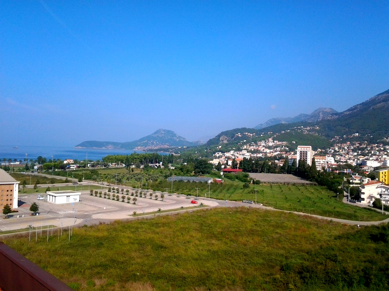 Panoramski pogled na more, planine i grad Bar u Crnoj Gori iz prozora stana, zelena polja i parking u prvom planu.
