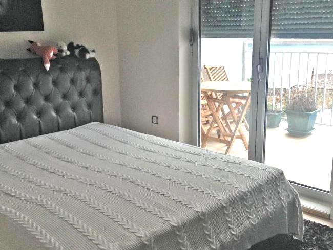 Schlafzimmer mit Doppelbett und Zugang zur Terrasse in einer Wohnung in Dobrota, Montenegro. Blick auf den Balkon mit Möbeln.