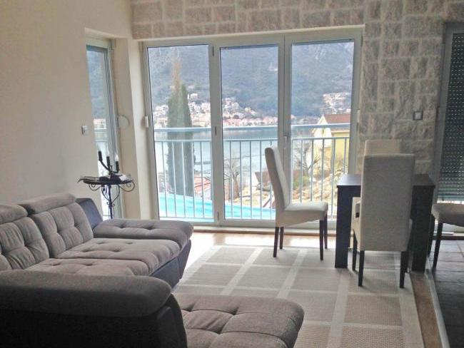Wohnzimmer in einer Wohnung in Dobrota, Montenegro: Panoramablick auf das Meer, Steinwandverkleidung, weiches Sofa und Essbereich.