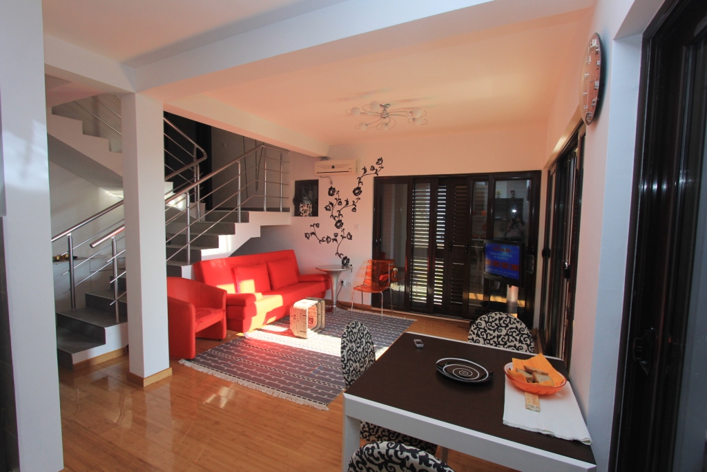 Wohnzimmer mit rotem Sofa und Treppe in einer Wohnung in Rafailovići, Montenegro: modernes Interieur mit Essbereich.