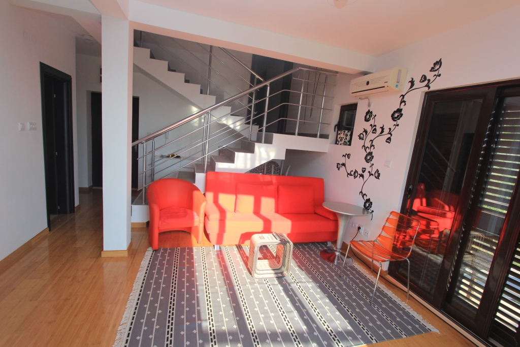 Wohnzimmer in einer Wohnung in Rafailovici, Montenegro: rote Möbel, Treppe mit Geländer und Panoramaverglasung.