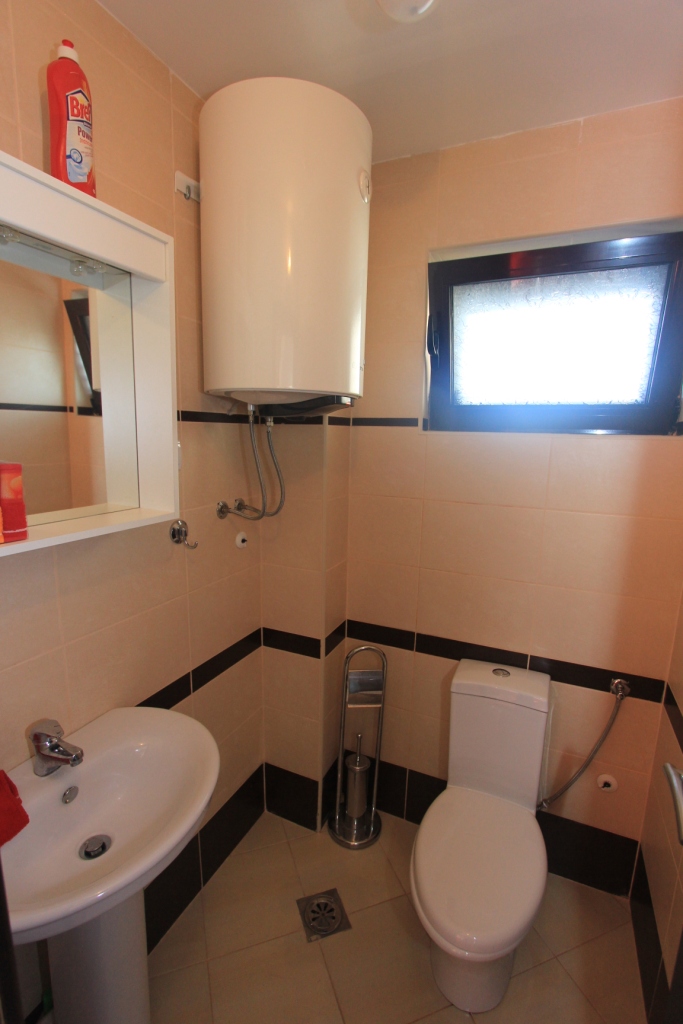 Badezimmer in der Wohnung, Rafailovići, Montenegro: beige Fliesen, Boiler, Waschbecken, Toilette und Fenster.