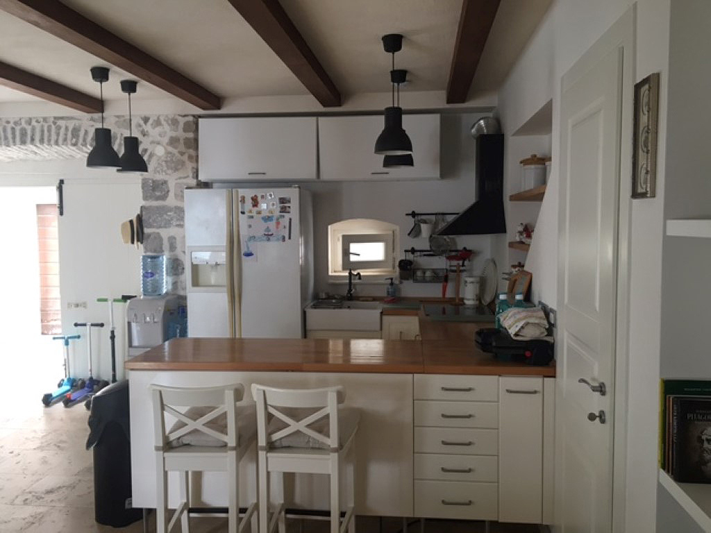 Kuhinja sa barskim pultom i kamenim zidom u enterijeru vile u Perastu, Crna Gora. Savremeni nameštaj i dekor.