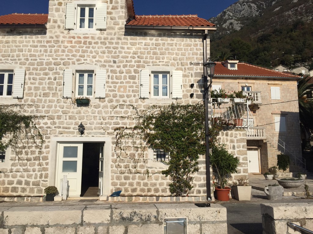 Tradicionalna kamena vila u Perastu, Crna Gora: fasada od svetlog kamena, beli kapci i pogled na planine.