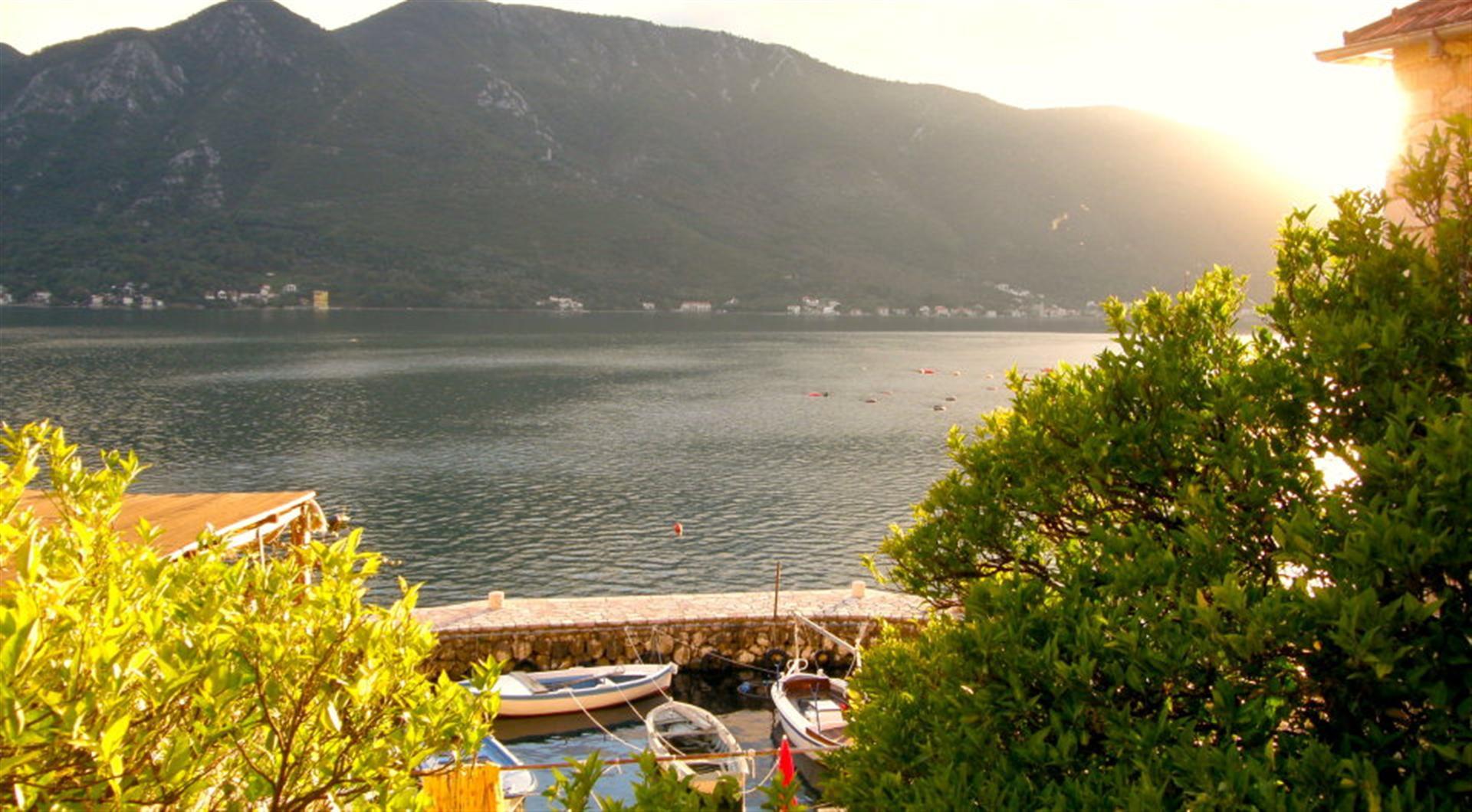 Karadağ, Dražin Vrt’teki villanın terasından Kotor Körfezi ve dağ manzarası: ön planda teknelerin bağlı olduğu iskele ve yeşillik.