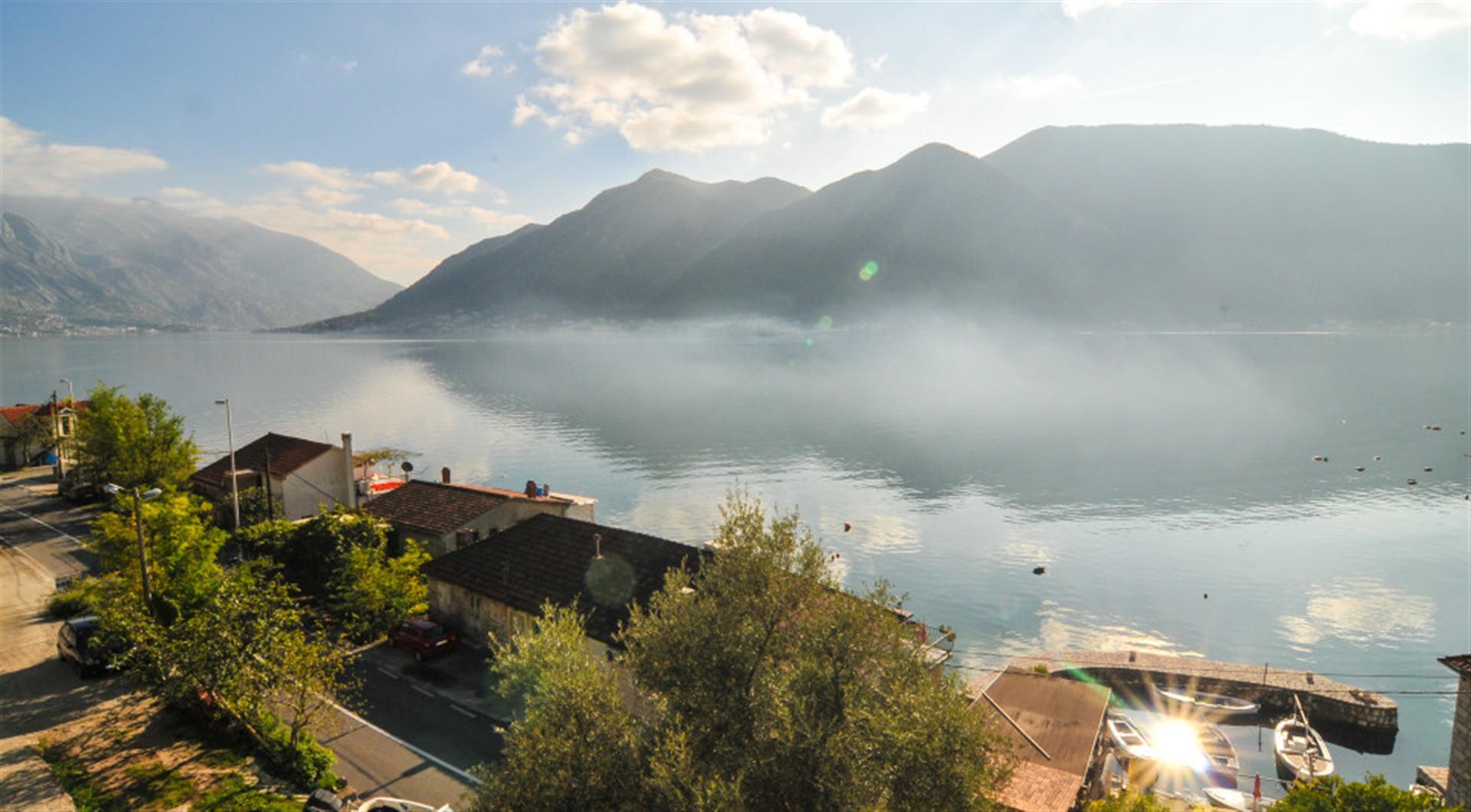 Karadağ, Dražin Vrt’teki villadan Kotor Körfezi ve dağların panoramik manzarası: kıyı şeridi ve tekne iskelesi.