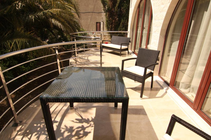 Spacieuse terrasse de la villa à Lastva, Monténégro : mobilier en osier, table en verre et garde-corps en acier inoxydable.