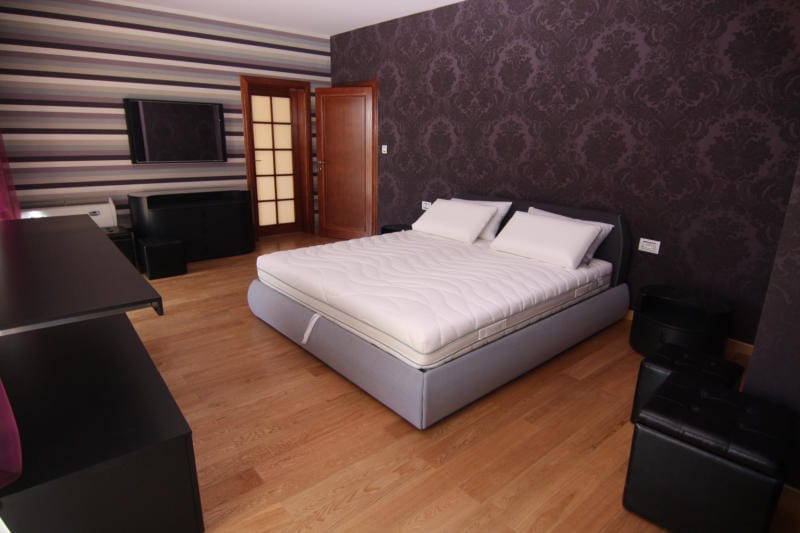 Chambre spacieuse avec lit double dans une villa, Lastva, Monténégro : papier peint sombre, parquet en bois et mobilier moderne.