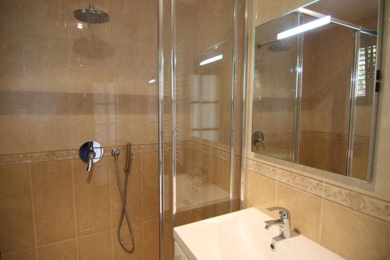 Salle de bains avec cabine de douche et carrelage clair dans une villa à Lastva, Monténégro. Sanitaires modernes et miroir.