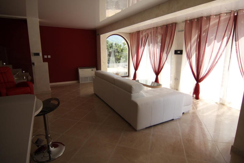 Salon avec canapé blanc et baies vitrées panoramiques dans une villa à Lastva, Monténégro : intérieur moderne avec murs rouges.