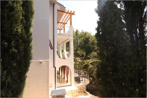 Façade d’une villa moderne à Lastva Grbaljska, Monténégro : terrasses en arc, baies panoramiques et jardin avec cyprès.