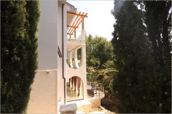 Façade d’une villa moderne à Lastva Grbaljska, Monténégro : terrasses en arc, baies panoramiques et jardin avec cyprès.