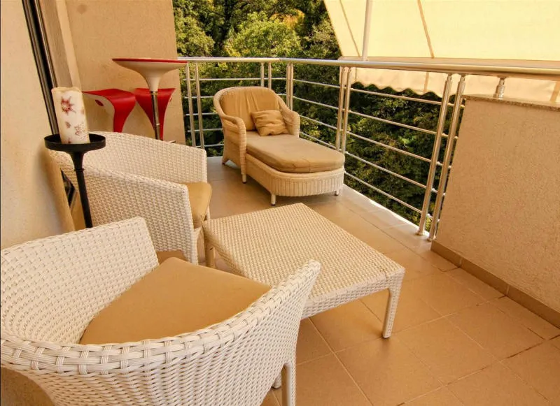 Sonniger Balkon mit weißen Korbsesseln, einem Tisch und einer Chaiselongue.