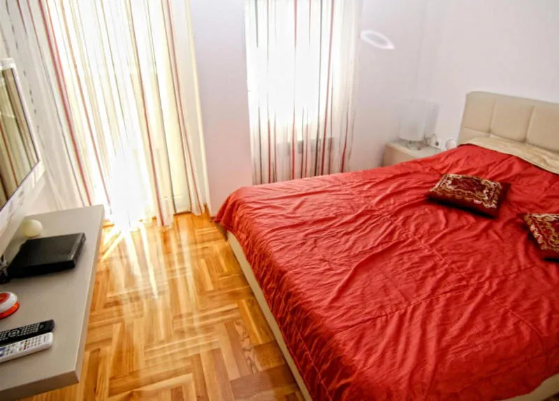 Schlafzimmer mit einem großen Bett mit roter Tagesdecke, Holzboden und TV-Ständer