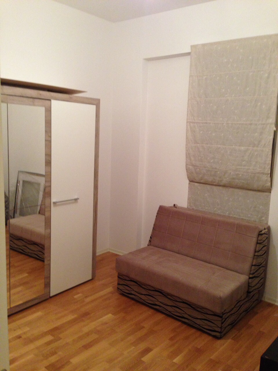 Schlafzimmer in einer Wohnung in Bečići, Montenegro: heller Kleiderschrank mit Spiegel, Schlafsofa und römische Rollos, Parkettboden.