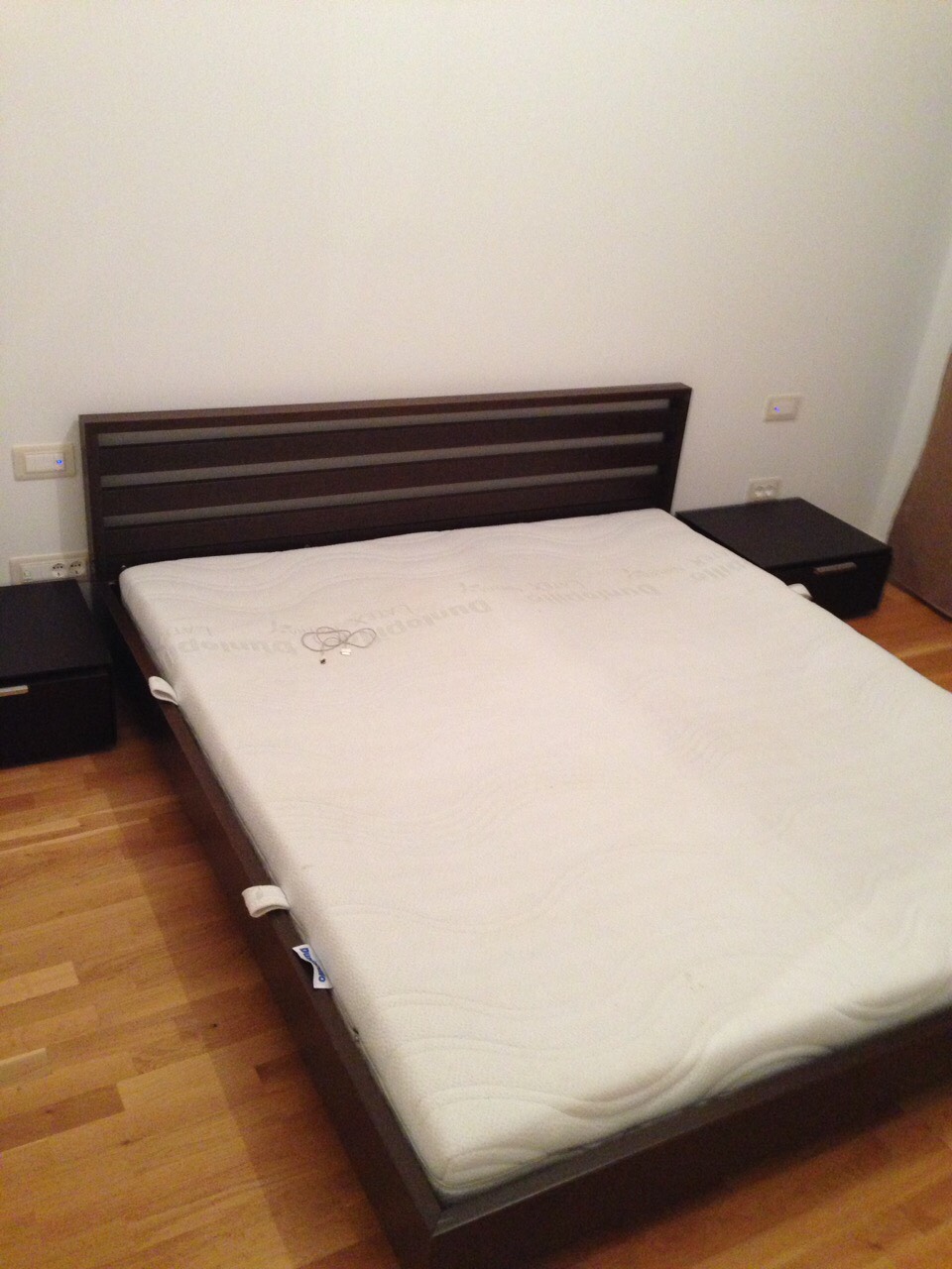 Doppelbett mit dunklem Kopfteil und Nachttischen im Schlafzimmer einer Wohnung in Bečići, Montenegro. Parkettboden.
