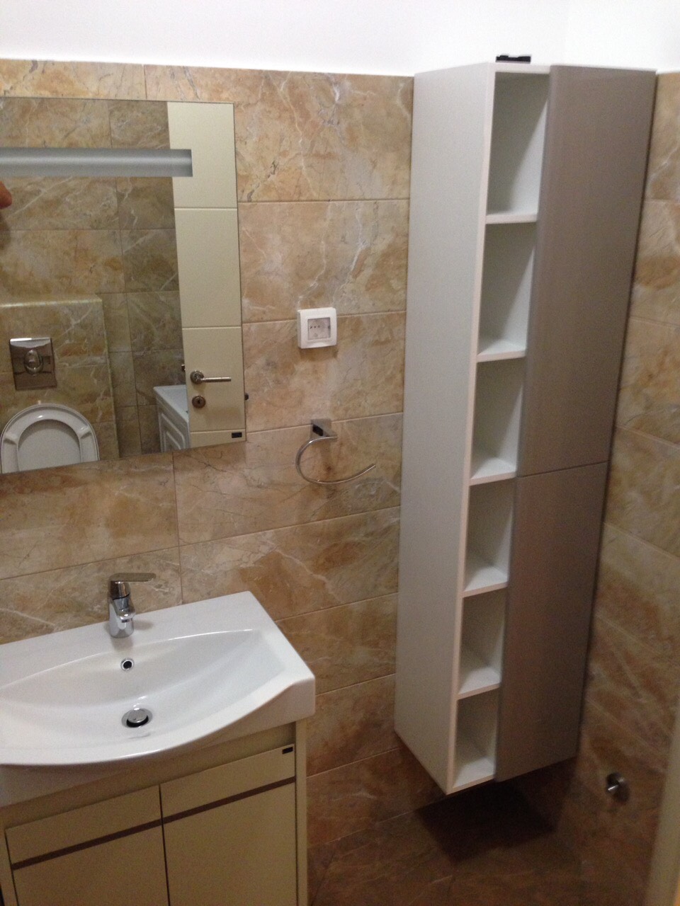 Badezimmer in einer Wohnung in Bečići, Montenegro: weißes Waschbecken, Hängeschrank und Wände mit beigen Fliesen.