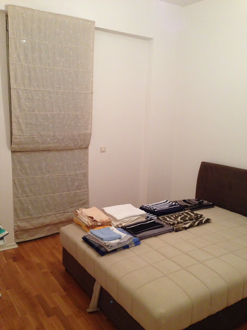 Schlafzimmer in einer Wohnung in Bečići, Montenegro: Doppelbett mit gepolstertem Kopfteil, helle Römische Vorhänge und Parkettboden.