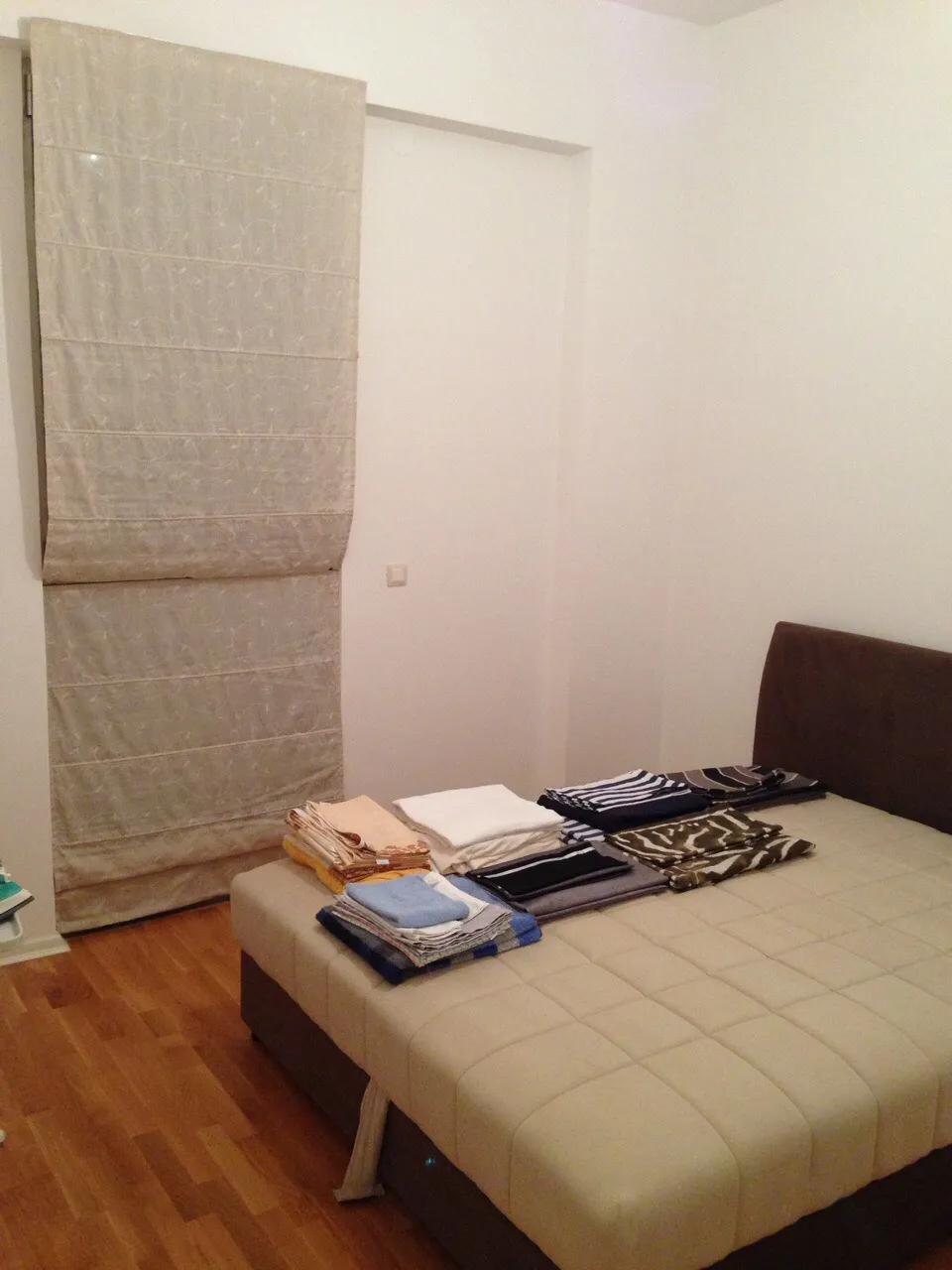 Schlafzimmer in einer Wohnung in Bečići, Montenegro: Doppelbett mit gepolstertem Kopfteil, helle Römische Vorhänge und Parkettboden.