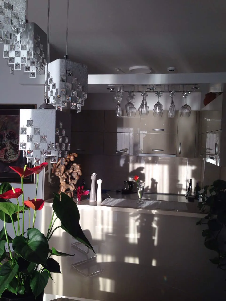 Moderne Küche in einer Wohnung in Bečići, Montenegro: glänzende Fronten, Pendelleuchten und ein Gläserhalter.