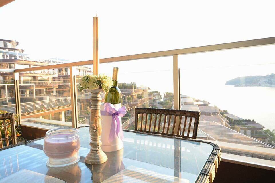 Balcon avec mobilier en osier et vue sur la mer dans un appartement à Bečići, Monténégro. Table décorée et baies vitrées panoramiques.