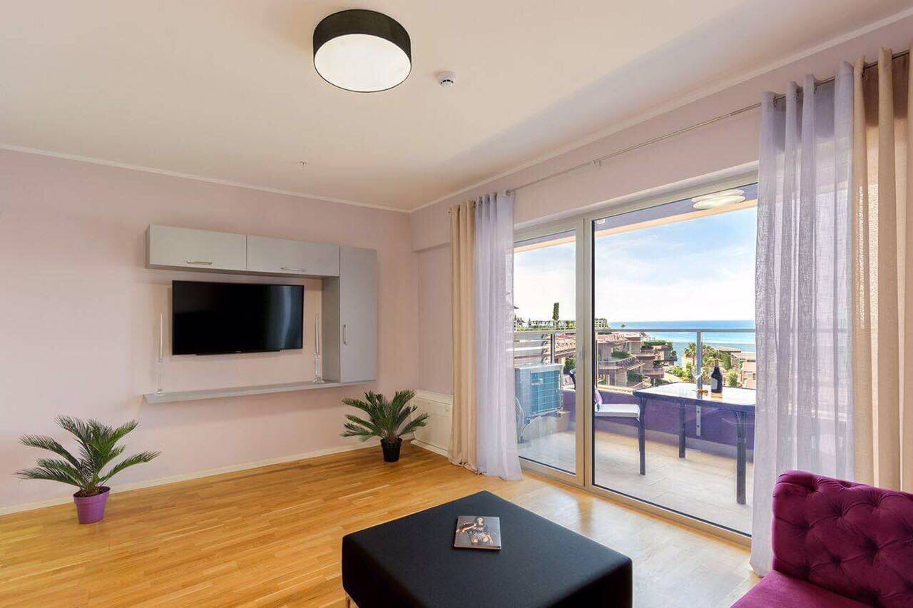 Salon dans un appartement à Bečići, Monténégro : mobilier moderne, espace TV et vue panoramique sur la mer depuis la terrasse.