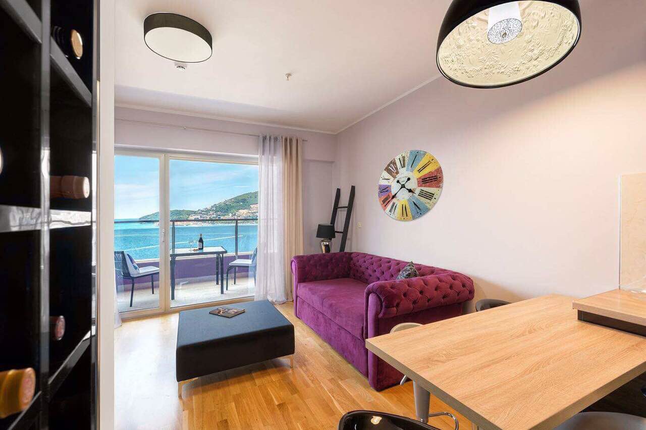 Salon avec canapé violet et vue sur la mer dans un appartement à Bečići, Monténégro : intérieur moderne avec terrasse.