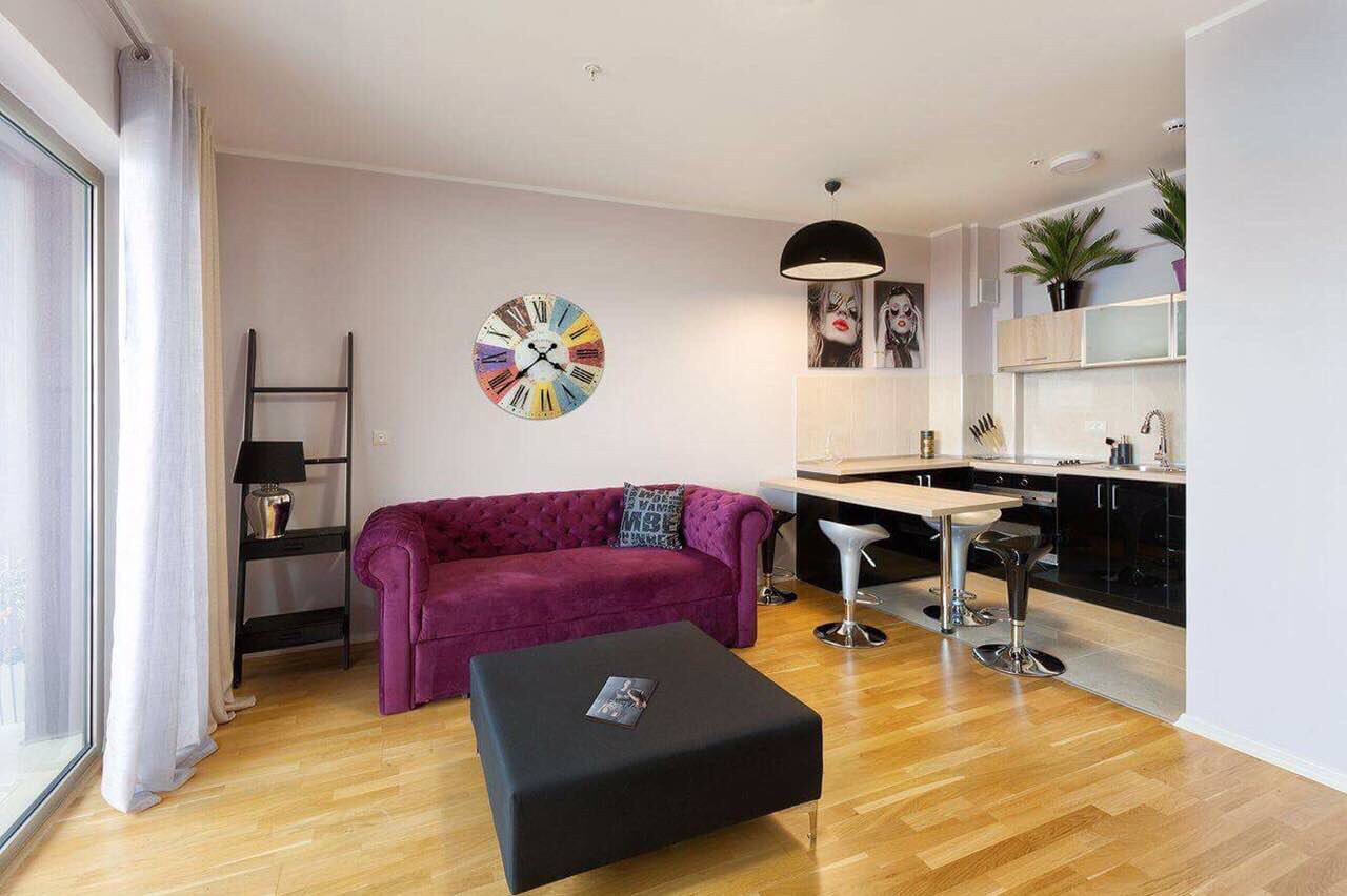 Salon moderne avec canapé violet et cuisine dans un appartement à Bečići, Monténégro : intérieur élégant avec parquet.