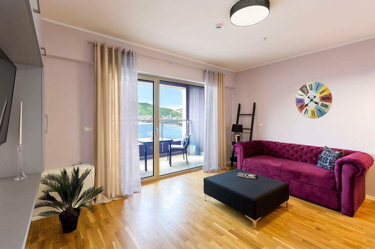 Salon dans un appartement à Bečići, Monténégro : canapé violet, vue panoramique sur la mer et accès à la terrasse.