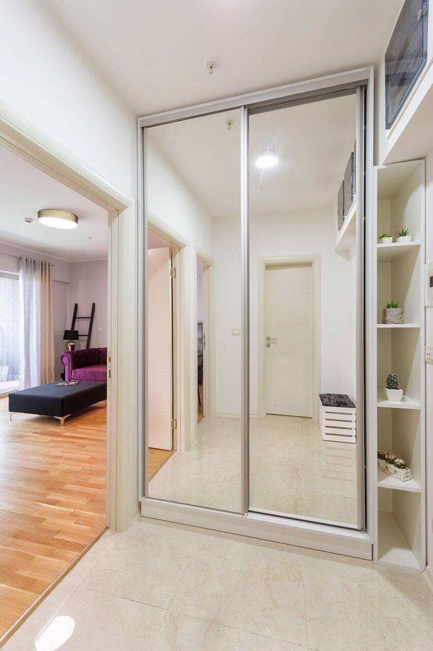 Entrée avec placard coulissant miroir et étagères ouvertes dans l’appartement, Bečići, Monténégro. Vue sur le salon avec parquet.