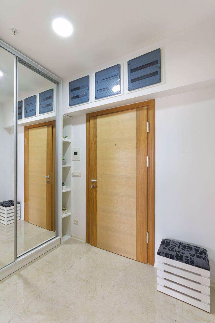 Entrée d’un appartement à Bečići, Monténégro : finition claire, placard intégré avec miroir et porte d’entrée en bois.