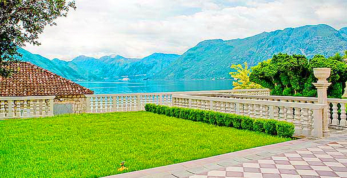 Blick auf die Bucht von Kotor von der Terrasse der Villa in Dobrota, Montenegro: gepflegter Rasen, steinerne Balustrade und Berge.