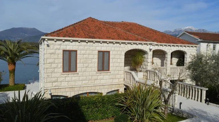 Zweigeschossige Steinvilla mit Ziegeldach und Terrasse in Tivat, Montenegro, am Meer mit Blick auf die Berge.