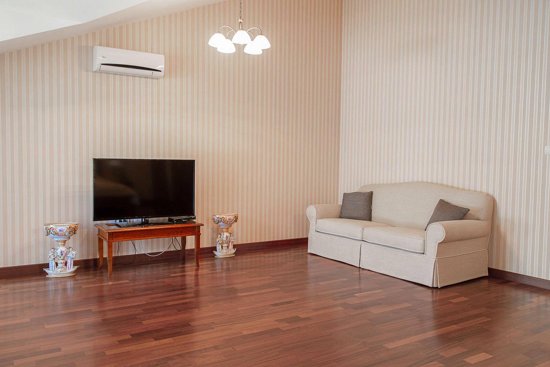 Salon dans une maison de ville à Lastva, Monténégro : canapé clair, TV, parquet, climatisation et décoration classique.