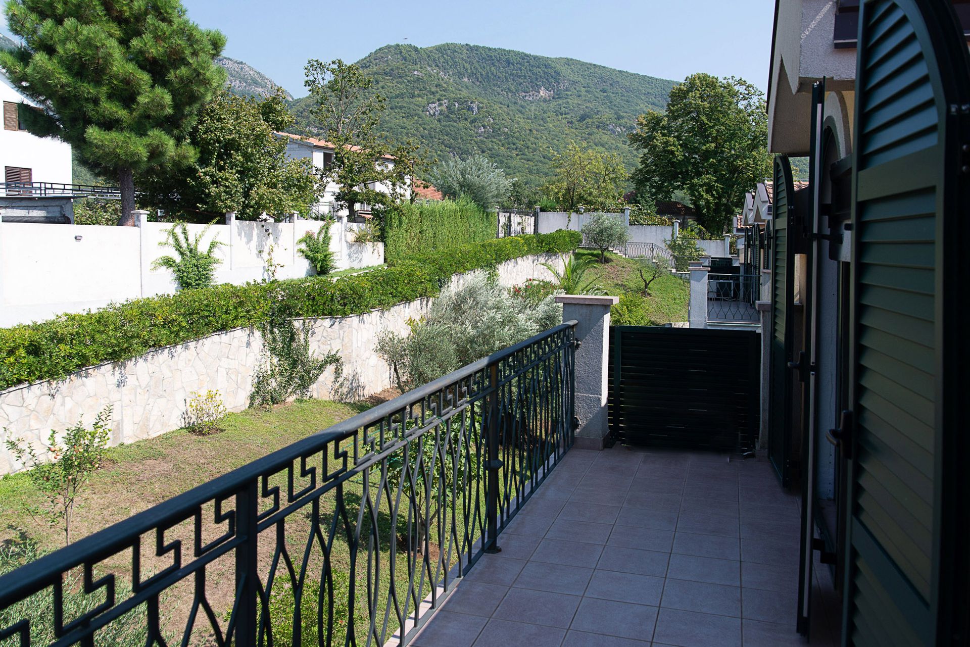 Balcon d’une maison de ville à Lastva, Monténégro, avec vue sur les montagnes verdoyantes, le jardin et une balustrade en fer forgé.