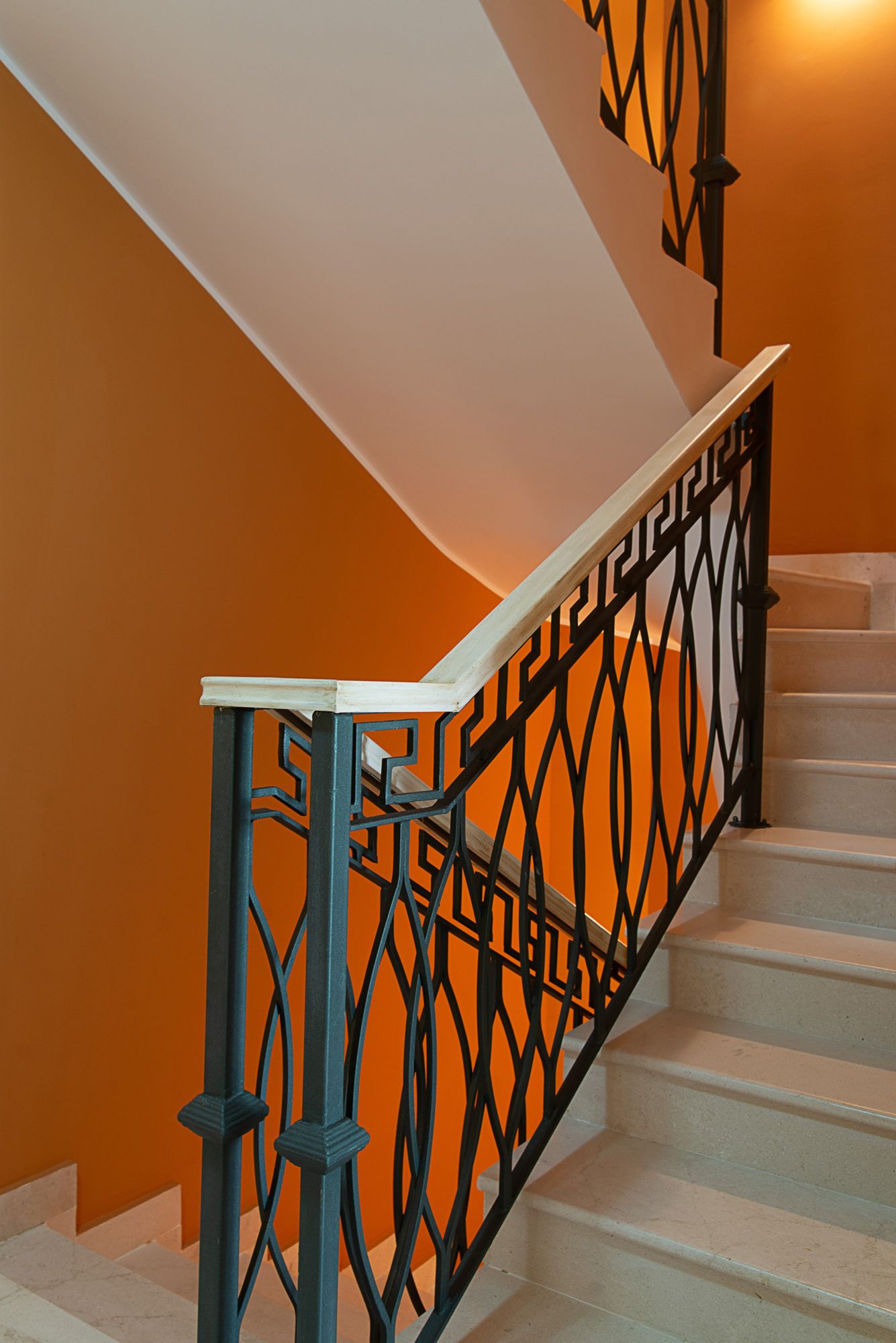 Escalier en marbre avec rampe en fer forgé dans une maison de ville à Lastva, Monténégro : intérieur aux murs orange.