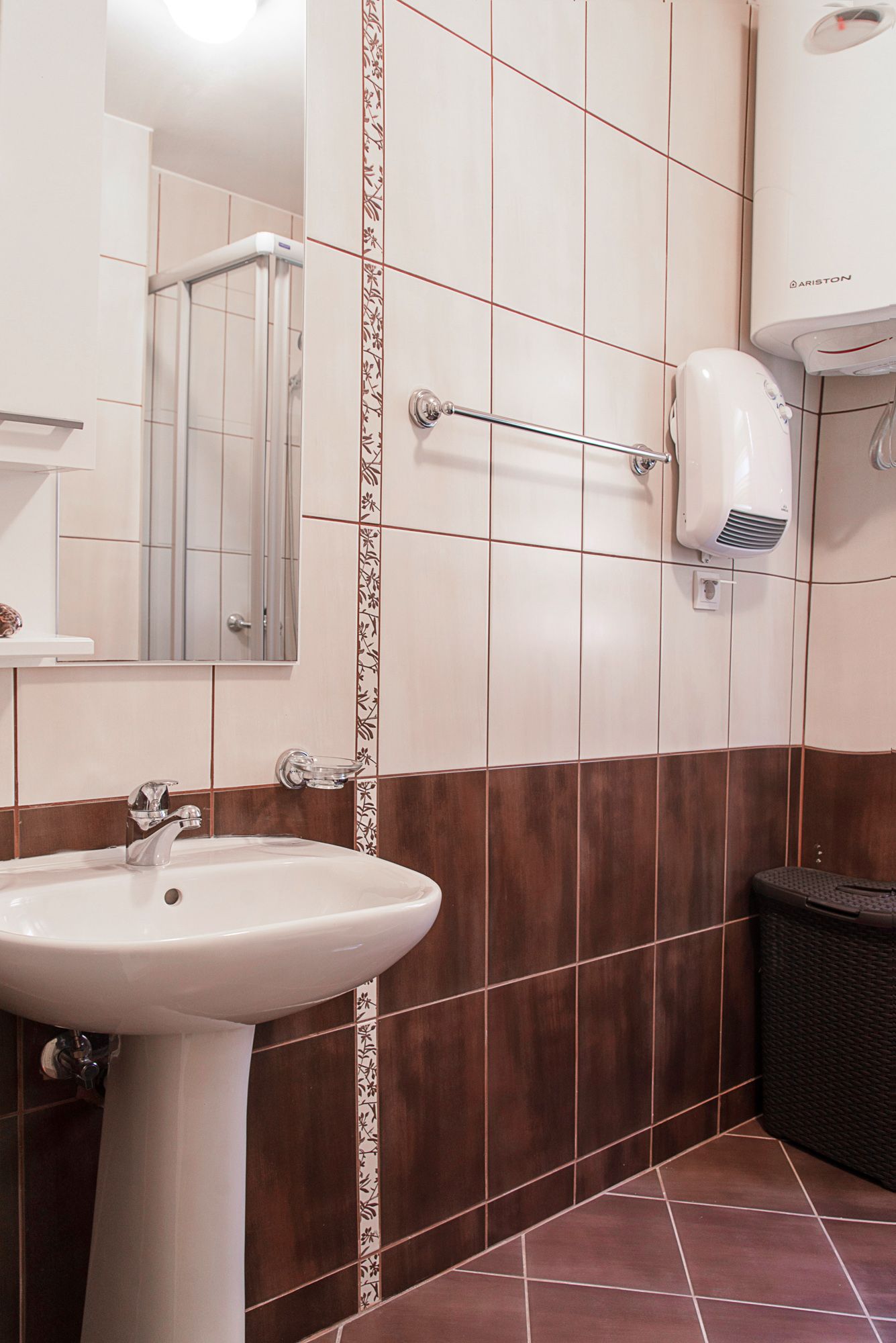 Salle de bain dans une maison de ville à Lastva, Monténégro : carrelage clair, lavabo, miroir et chauffe-eau Ariston.