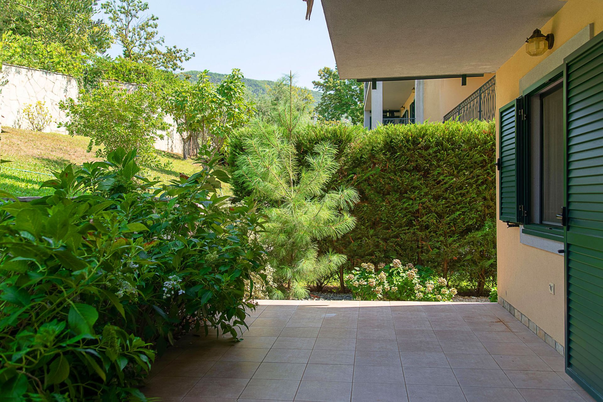 Terrasse chaleureuse d’une maison de ville à Lastva, Monténégro, avec accès à un jardin privé verdoyant et vue sur les montagnes.