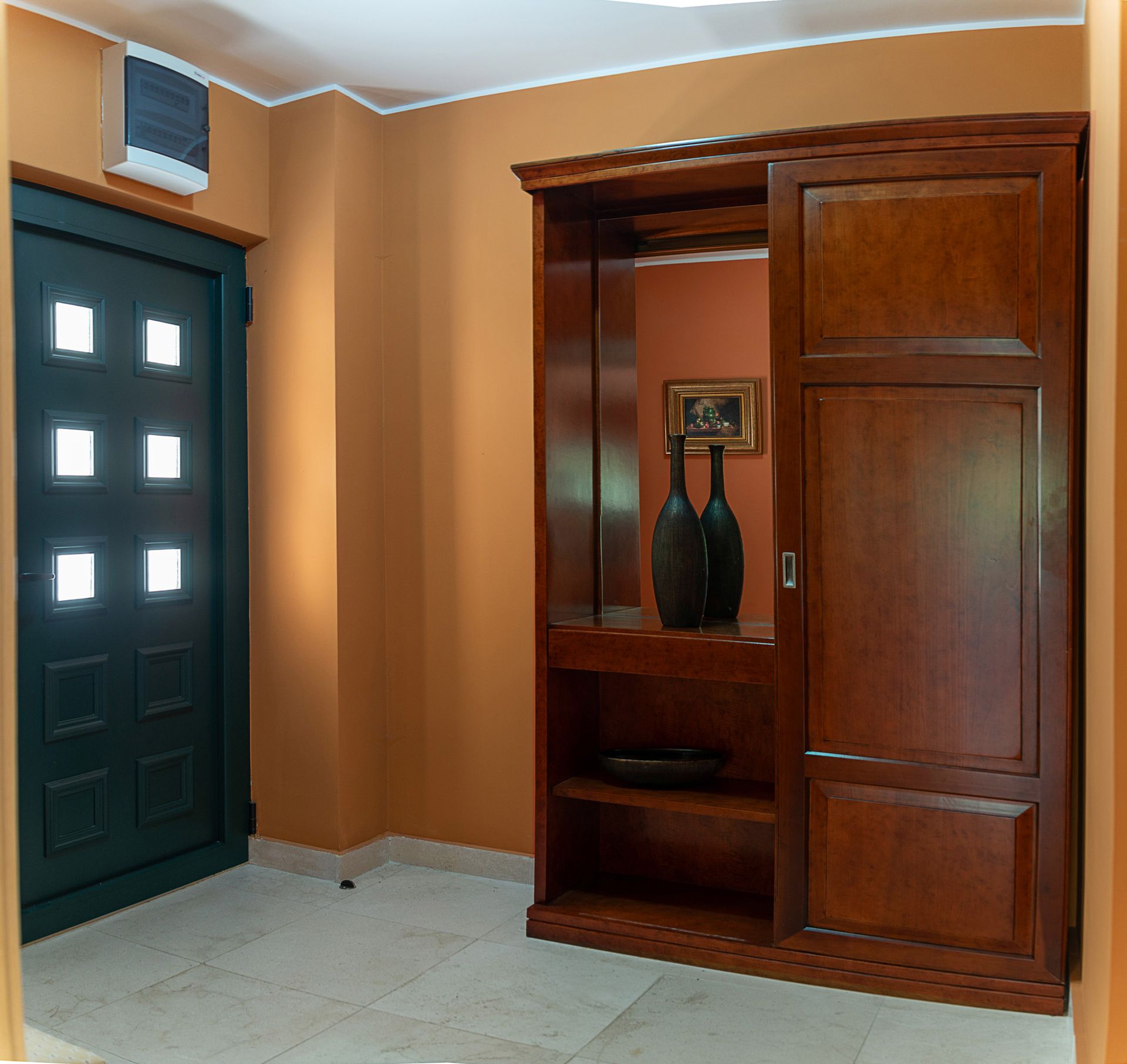 Entrée d’une maison de ville à Lastva, Monténégro : mobilier en bois foncé, miroir, décoration et porte d’entrée vitrée.