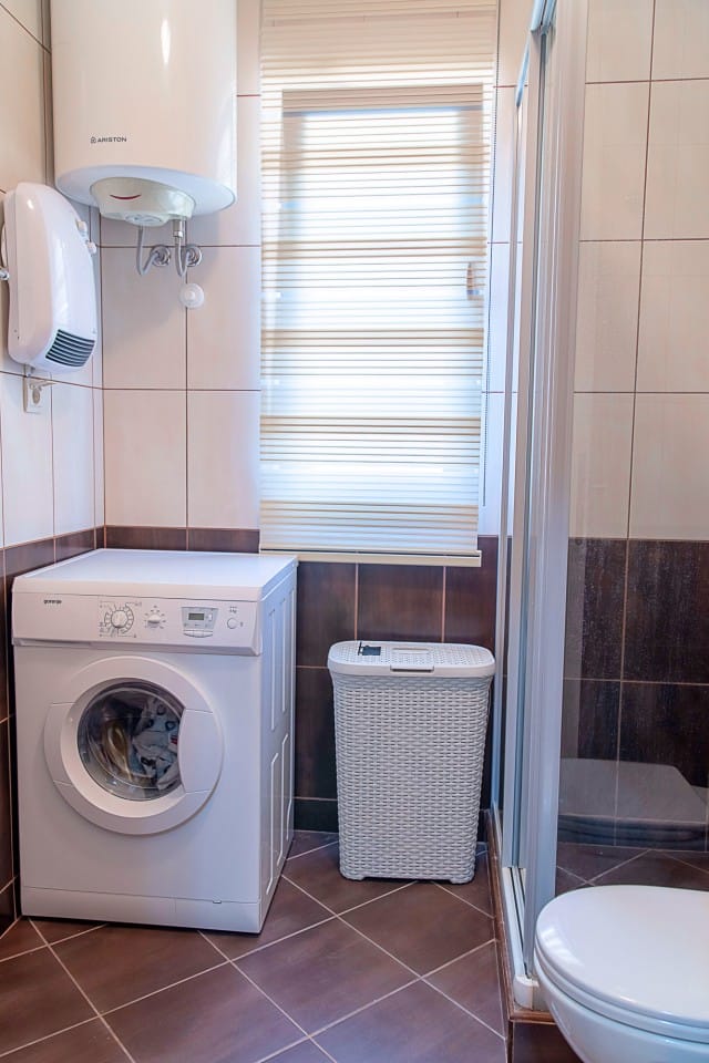 Salle de bains dans une maison de ville à Lastva, Monténégro : machine à laver, cabine de douche, chauffe-eau et revêtement en carrelage.