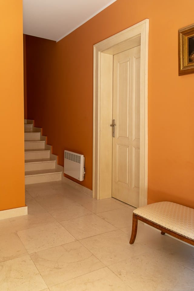 Intérieur de l’entrée d’une maison de ville à Lastva, Monténégro : escalier clair, carrelage beige et murs orange.