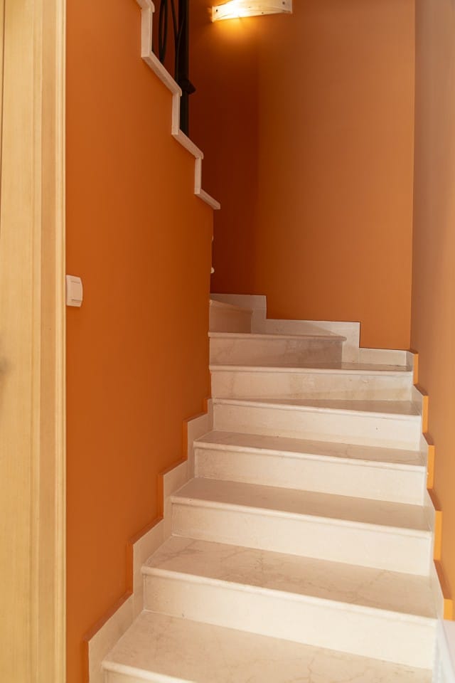 Escalier en marbre à l’intérieur d’une maison à Lastva, Monténégro : marches claires sur fond de murs orange vif.