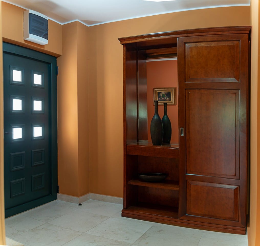Hall d’entrée d’une maison de ville à Lastva, Monténégro : mobilier en bois foncé, miroir et porte d’entrée vitrée.