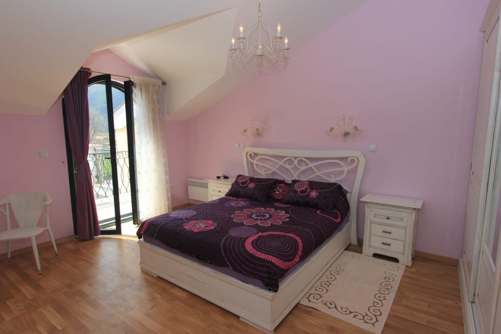 Chambre cosy dans une maison de ville à Lastva, Monténégro : lit double, mobilier clair et accès au balcon avec vue.