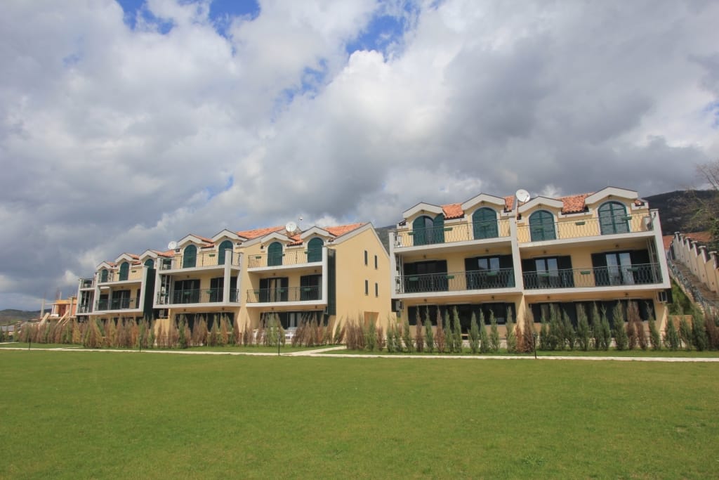 Maisons de ville de trois étages avec balcons et toit en tuiles, sur fond de montagnes à Lastva, Monténégro, avec une pelouse bien entretenue devant la maison.