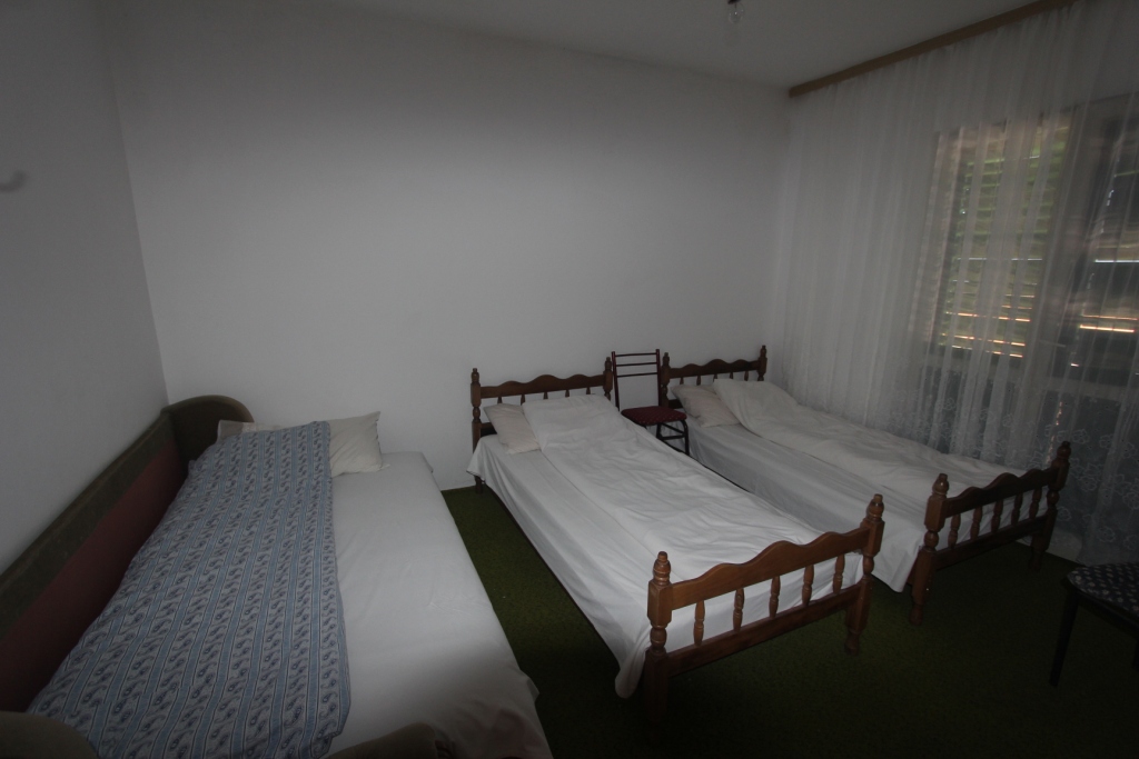 Schlafzimmer mit drei Einzelbetten in einem Haus in Radovići, Montenegro: klassische Möbel und Blick auf das Fenster mit Jalousien.
